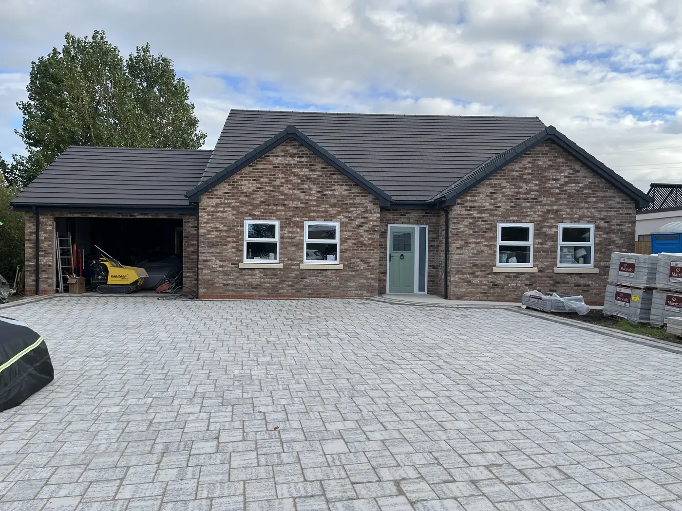 The completed bungalow from the driveway: brick elevation with an attached garage, green front door and block paved drive