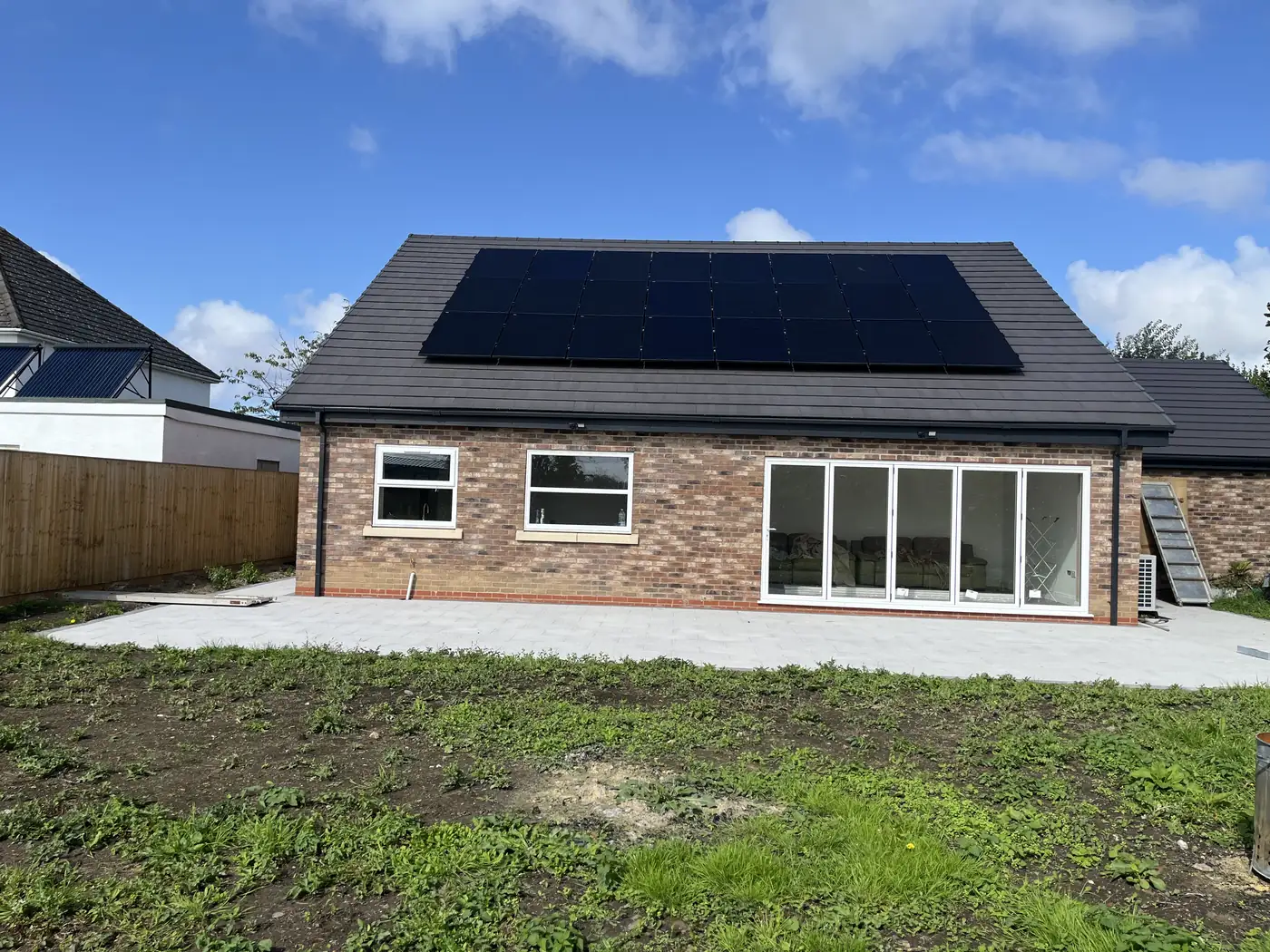 The completed bungalow from the garden: brick elevation, solar panels on the roof, and bi-fold doors onto a new patio
